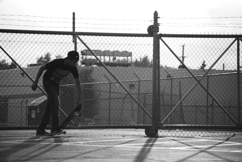 man skateboarding on pavement next to fence near industrial area