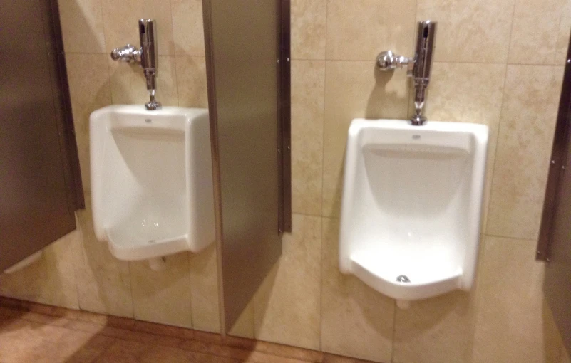 two urinals and mirrors inside of a bathroom stall