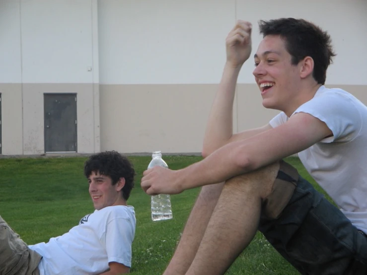 two young men playing with a bottle while sitting on the grass