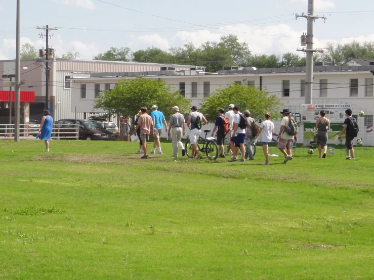 a group of people walk through a field next to buildings