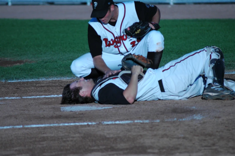 a baseball player laying on the ground and being helped by a catcher