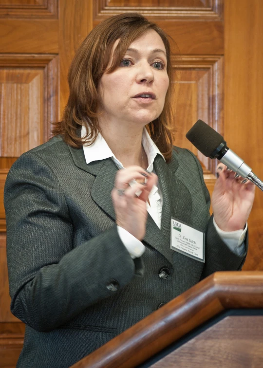 a woman wearing a green jacket speaking in front of a microphone