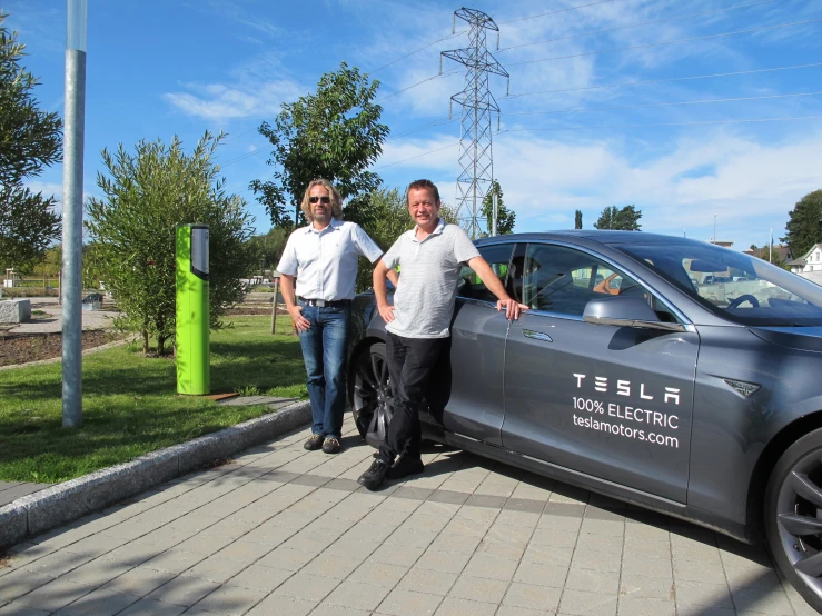 two people standing beside a car by some trees