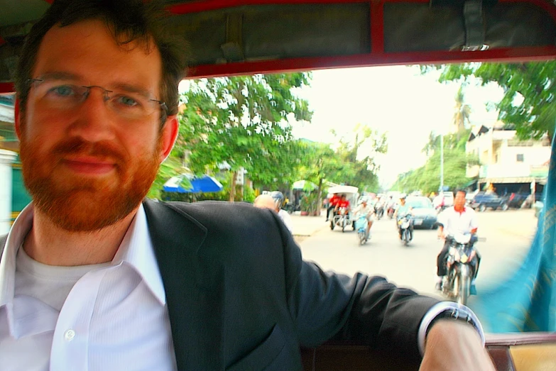 a man wearing glasses and a white shirt driving a car