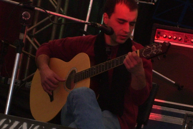 a man sitting on a stage holding an acoustic guitar