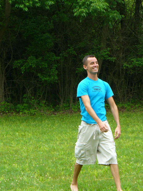 a man in blue shirt standing on grass next to trees