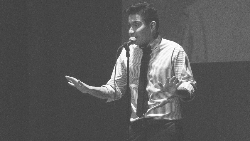 a man standing at a microphone, in front of an audience