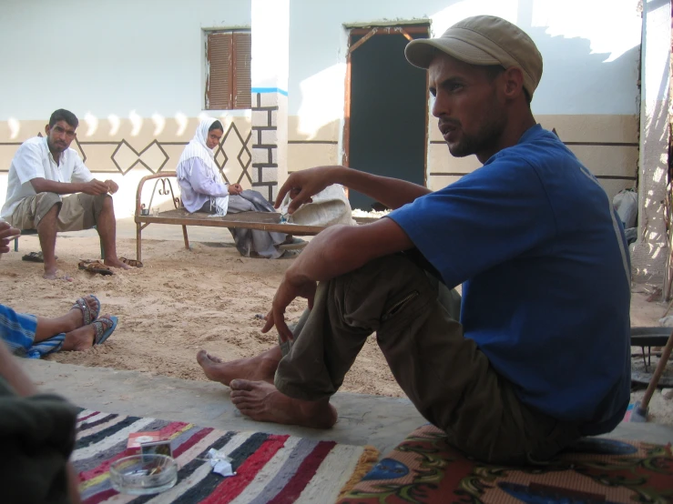 two people sitting on the ground while one man stands with soing in his hand