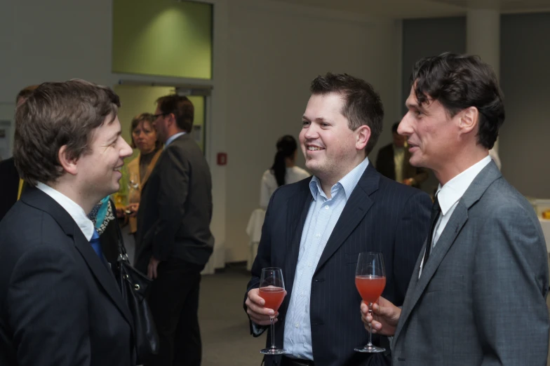 three men wearing suits and wine glasses with drinks in their hands