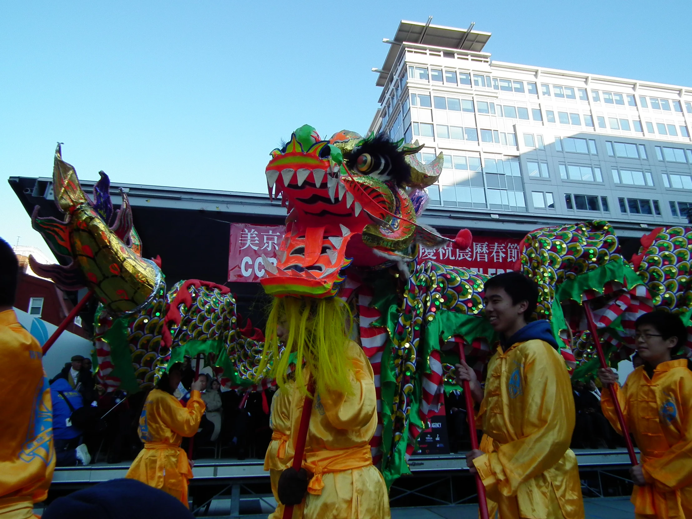 two dragon dancers with elaborate headdress and a building in the background