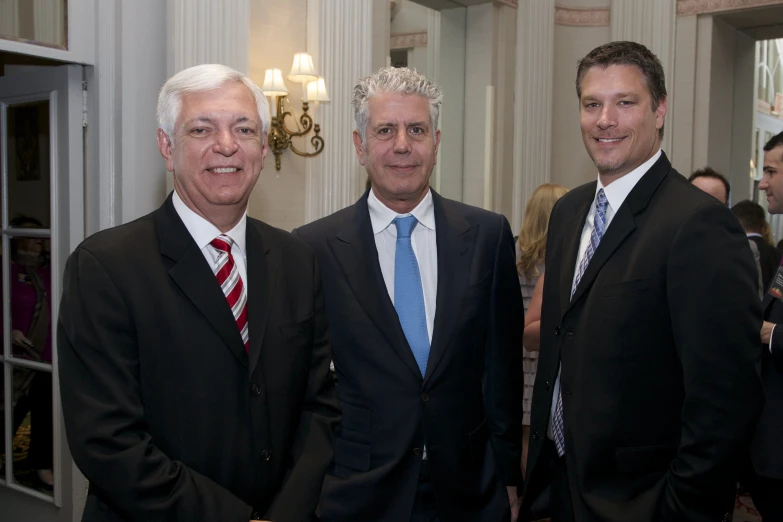 three men posing for the camera with a man in a tie