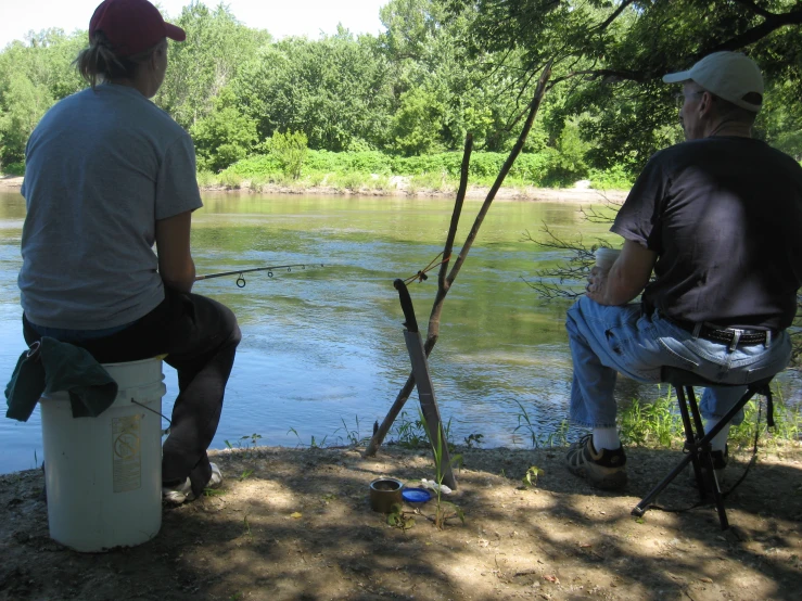 two men on a bench watching another man fishing on a lake