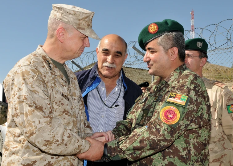 two men shake hands with two men in military clothing