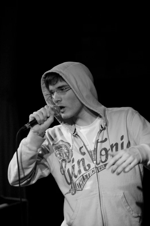 a man with a hoodie on is singing into a microphone