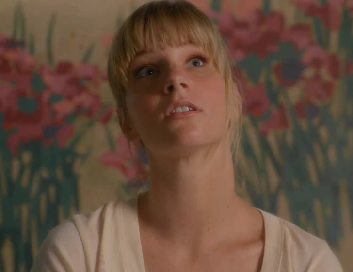 a woman stares to the right in front of a wall with flowers