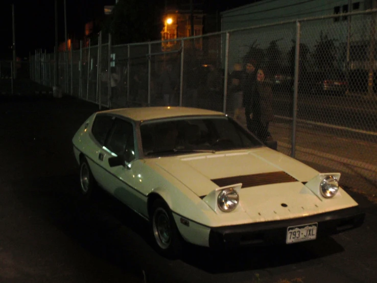 a white car with the hood up parked in front of a fence