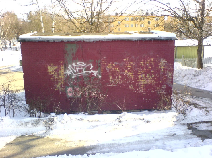 a red outhouse with graffiti covered in snow