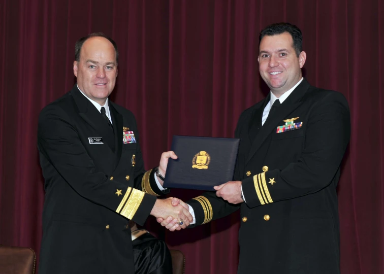 two men in uniforms shaking hands while standing