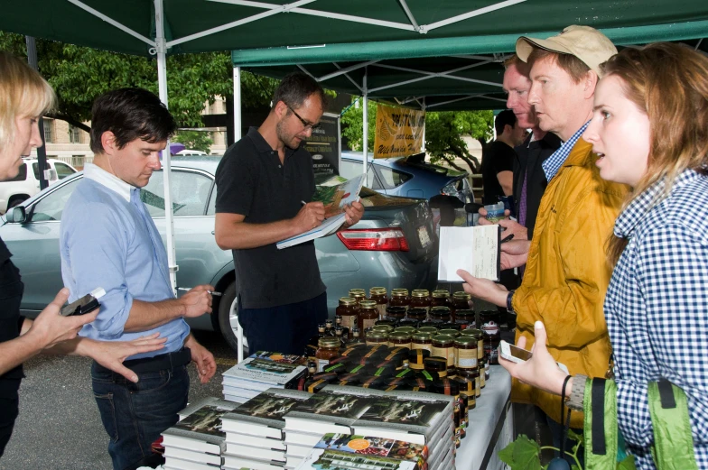 a group of people standing under a tent near a pile of books