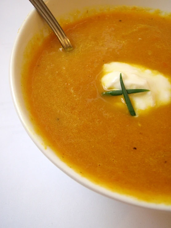 carrot soup in a white bowl with cream in the center