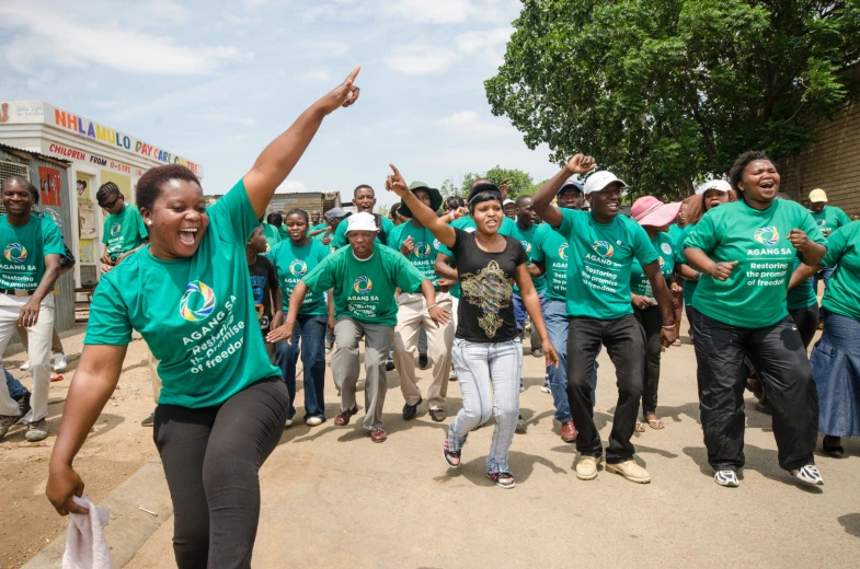 a woman with her arm raised up while a group of people in green shirts run behind