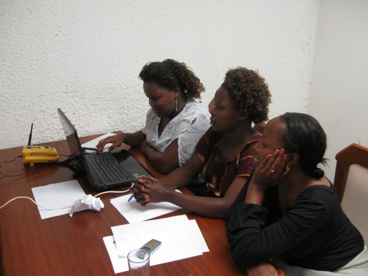 three girls sitting at a table with laptop computers