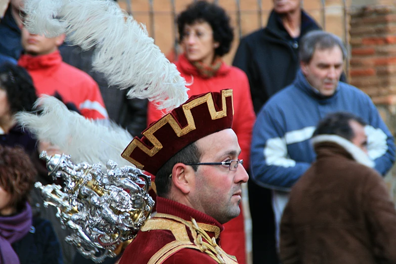 an old man wearing traditional greek garb stands in front of people at an event