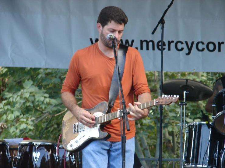 a man in orange shirt playing guitar and microphone