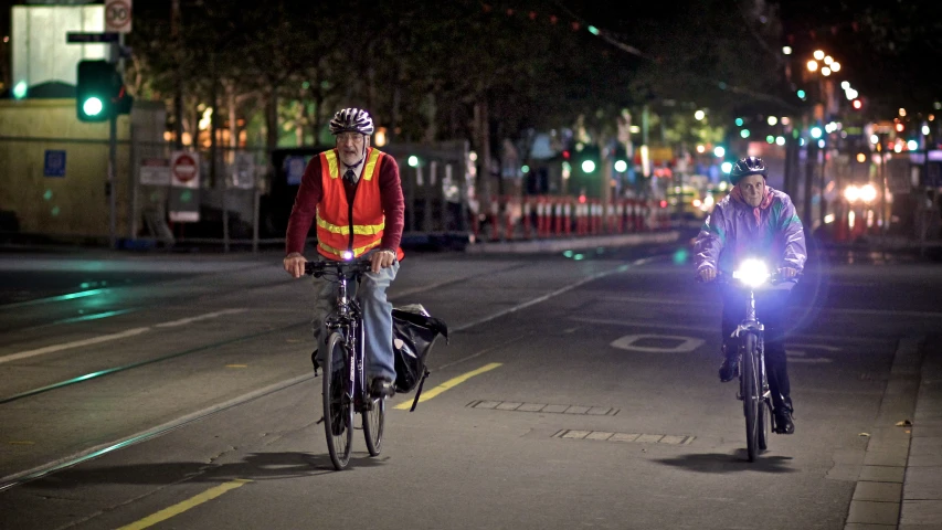 two bicyclists travel on the street at night