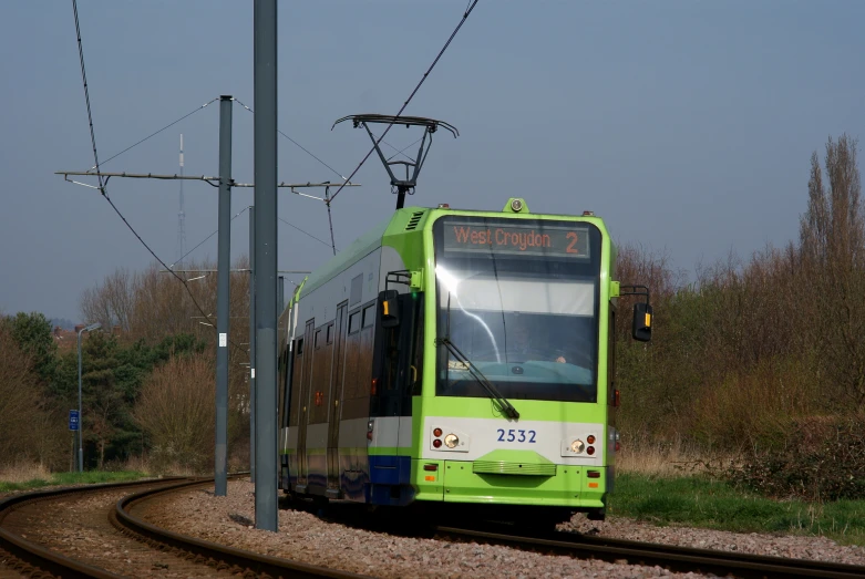 the large green bus is waiting to be on the train tracks