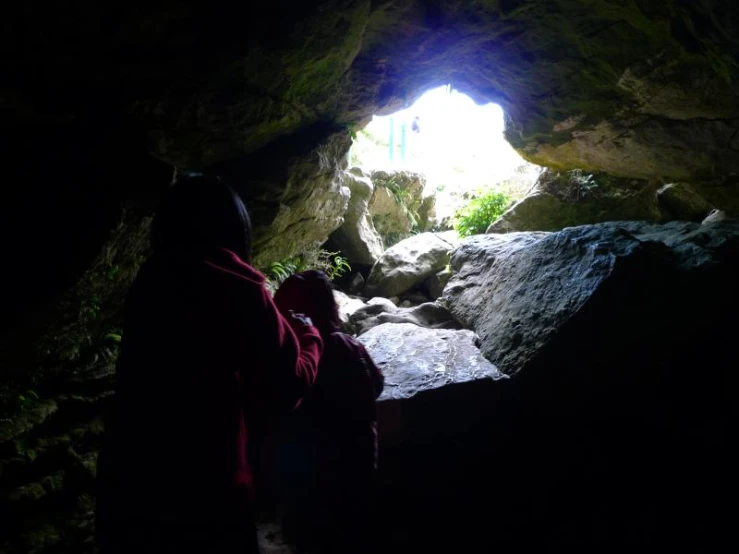 a woman in a red jacket standing by a cave door