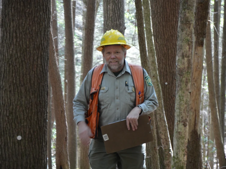 an older man wearing a hard hat and overalls in the woods