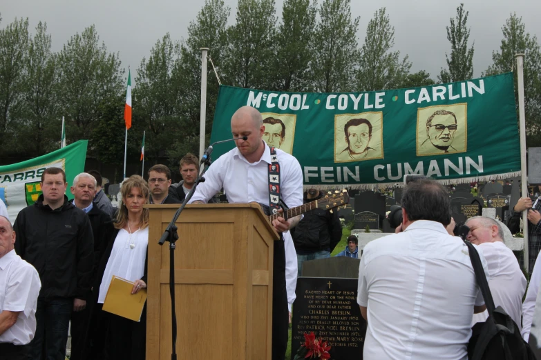 a man with a tie at a podium with a crowd in front of him