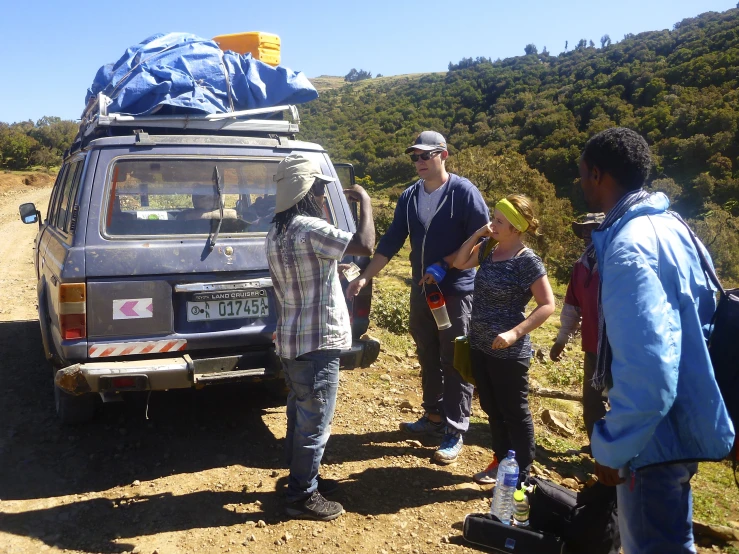 people are standing near a car with a sky blue tarp on top