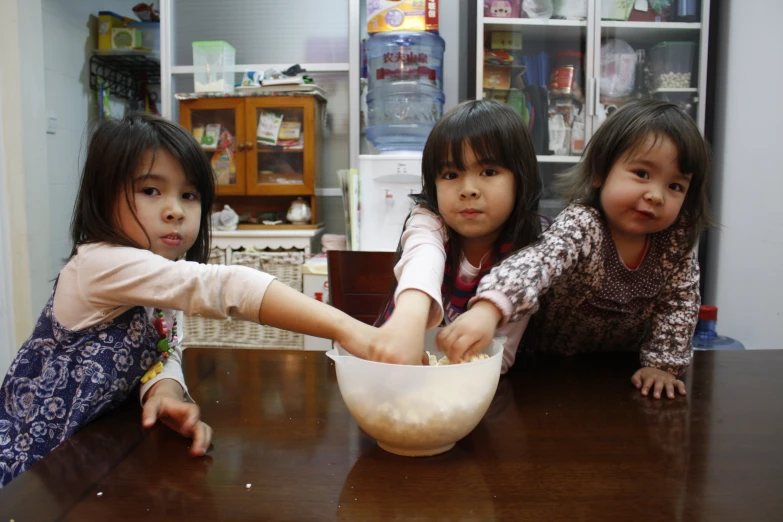 three little girls are mixing soing in a bowl