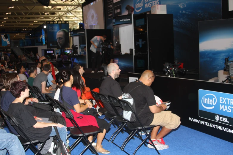 people in chairs at a large event watching soing on the wall