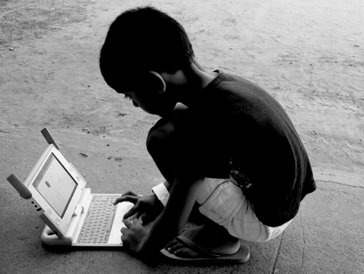 boy kneeling down with laptop on a pavement