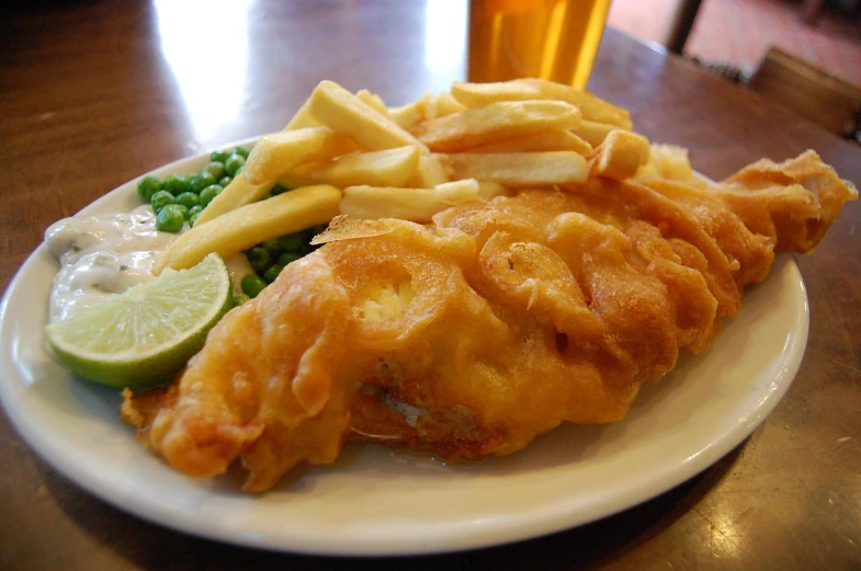 a white plate topped with fried fish, fries, and vegetables