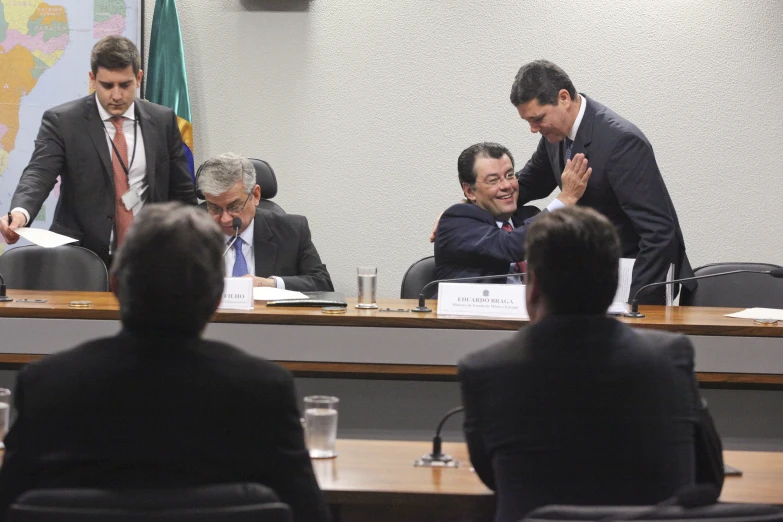 two men and one woman are smiling as they sit at a long table