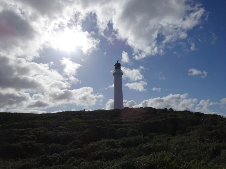 a small lighthouse on top of a hill with clouds overhead