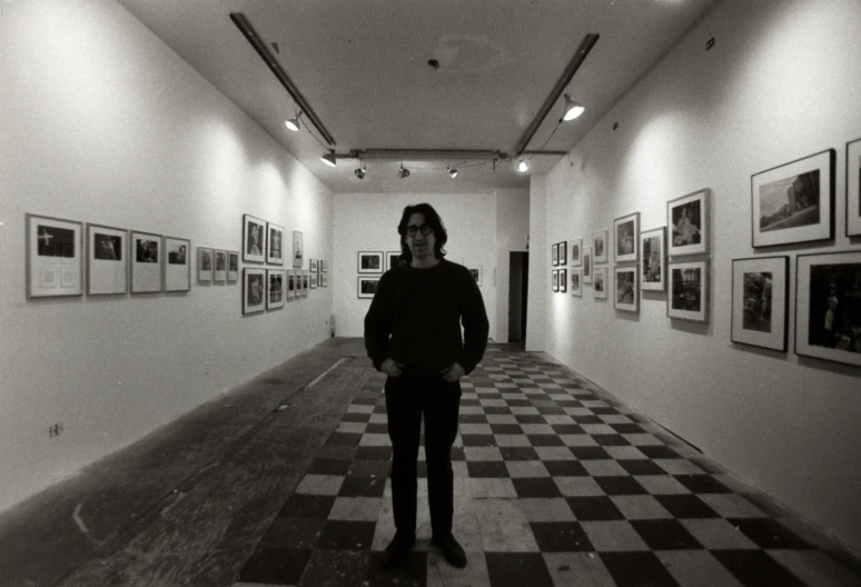 a man standing in a room with many framed pographs on the wall