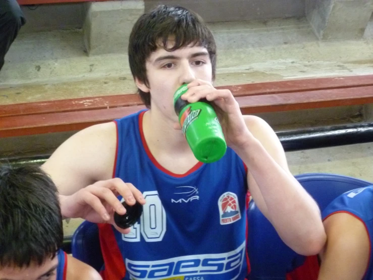 a young man drinks from a water bottle while sitting in front of his teammates