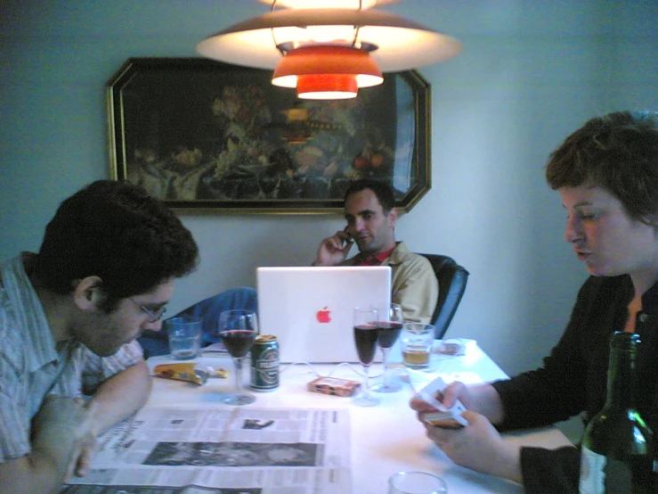 three men sitting at a table and looking at a magazine