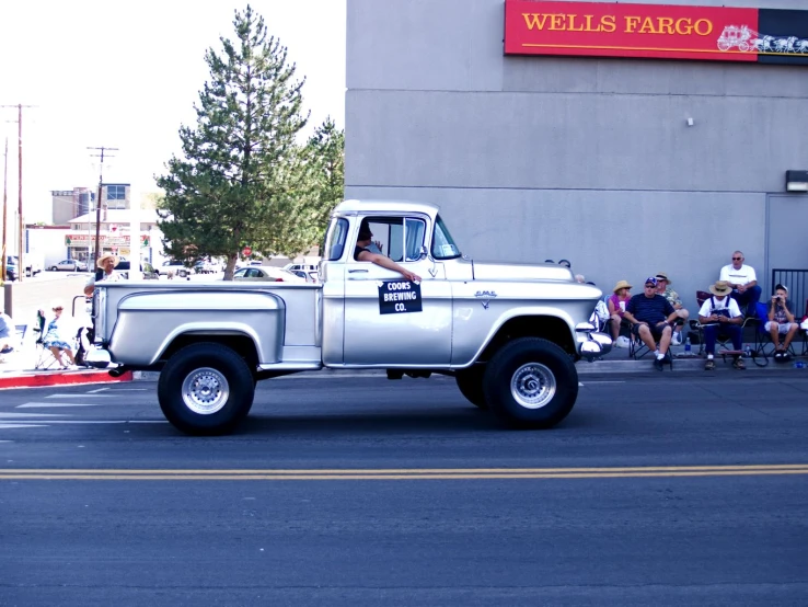 an old silver pick up truck driving past spectators