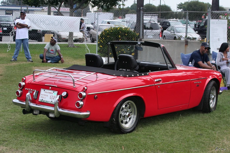 an older red convertible with two people on the grass