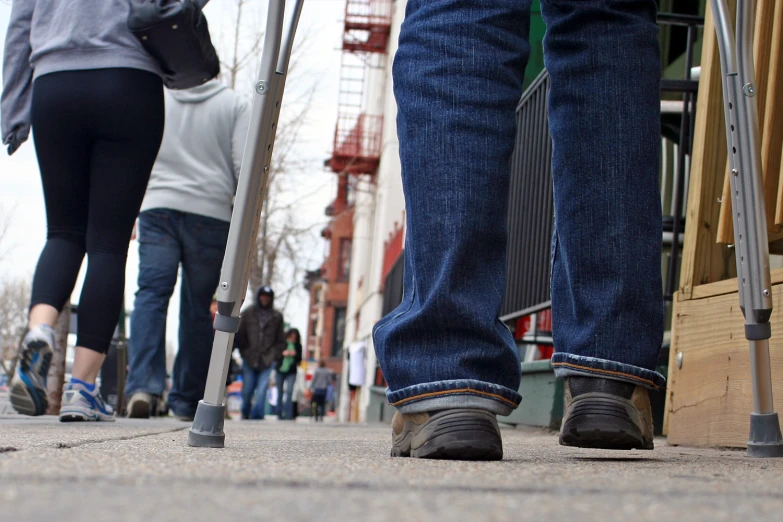 several people walking on the sidewalk with their crutches and canes