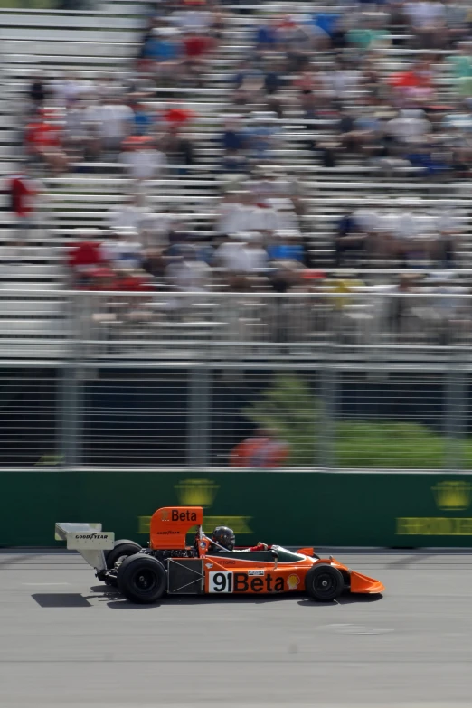 an orange car with a number 18 driving in front of people watching it