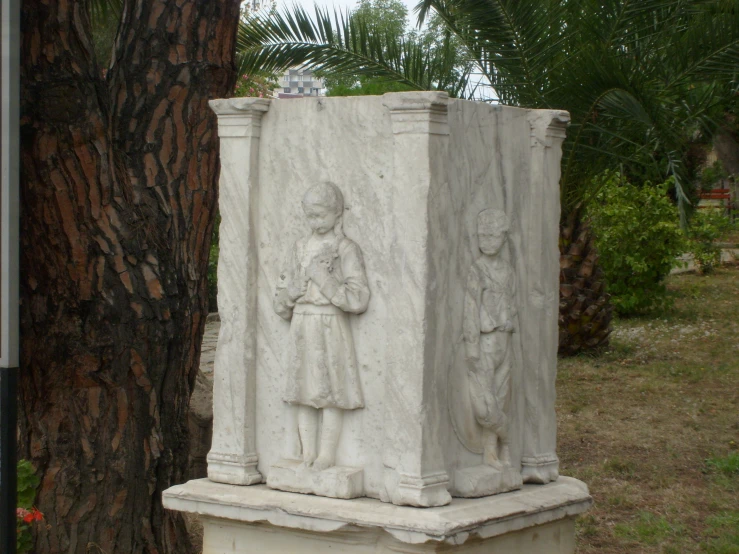 two cement statues sitting in a park next to a tree