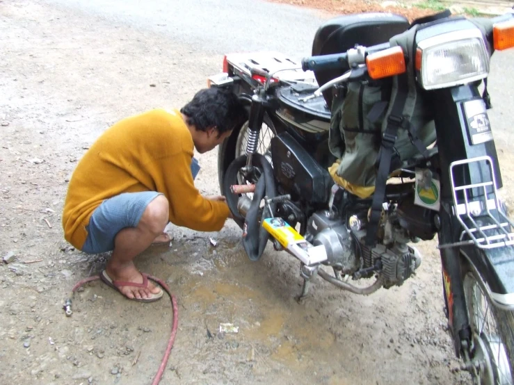 the man is repairing his motorcycle in the dirt