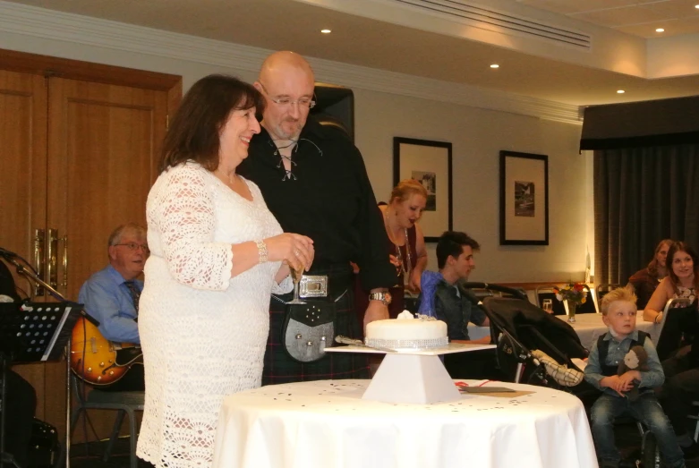 the man is standing next to a woman near a table with a cake on it